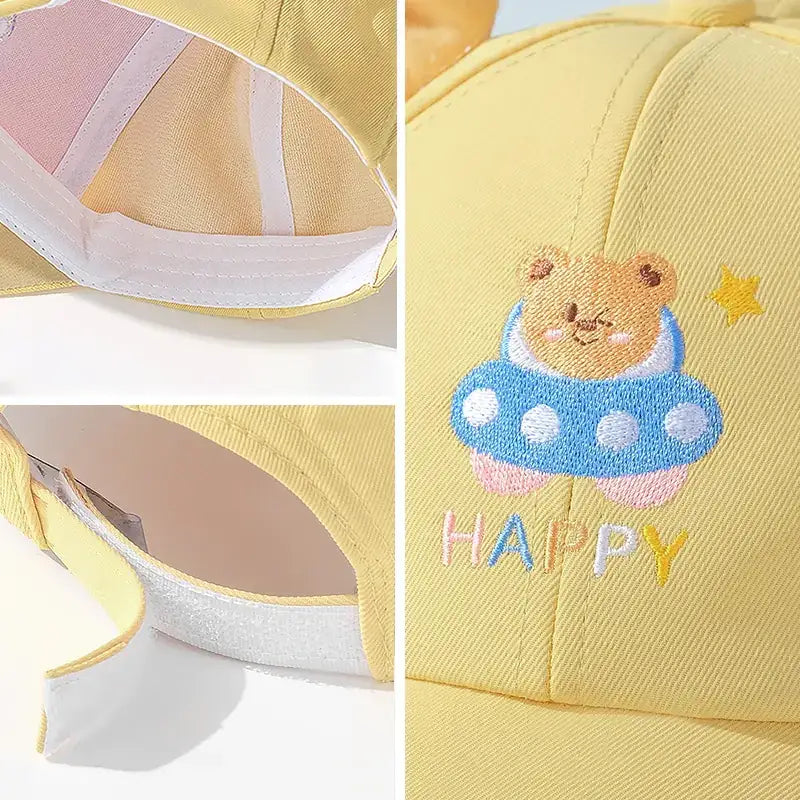 Yellow baseball cap featuring a cute embroidered bear in a blue ufo with white polka dots, accompanied by the word ’happy’ and a small star.