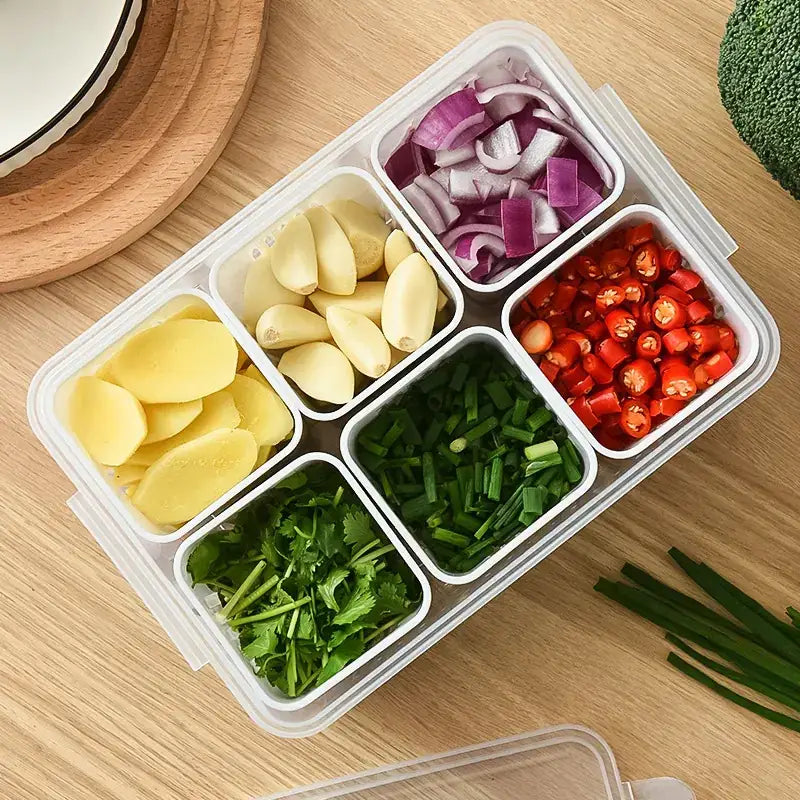 Clear plastic compartmentalized food storage container with white interior dividers holding chopped vegetables.