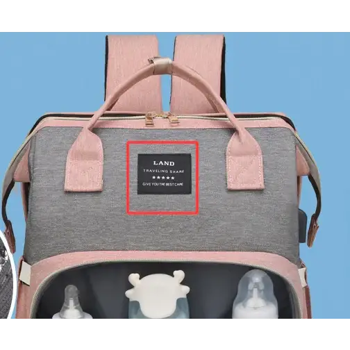 Pink and gray baby backpack with a black label that reads ’land traveling shape give you the best care.’