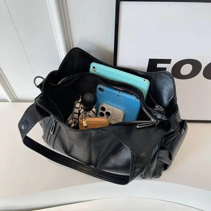Black leather crossbody bag with multiple compartments and zippers, filled with phones and accessories
