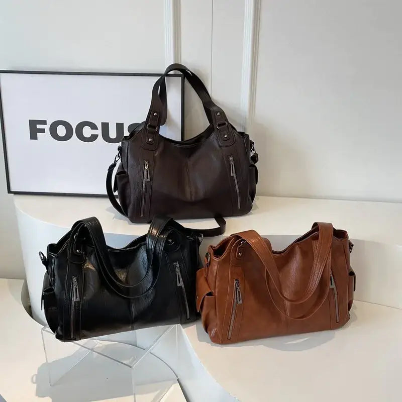 Black leather handbag with silver zippers and adjustable shoulder strap.