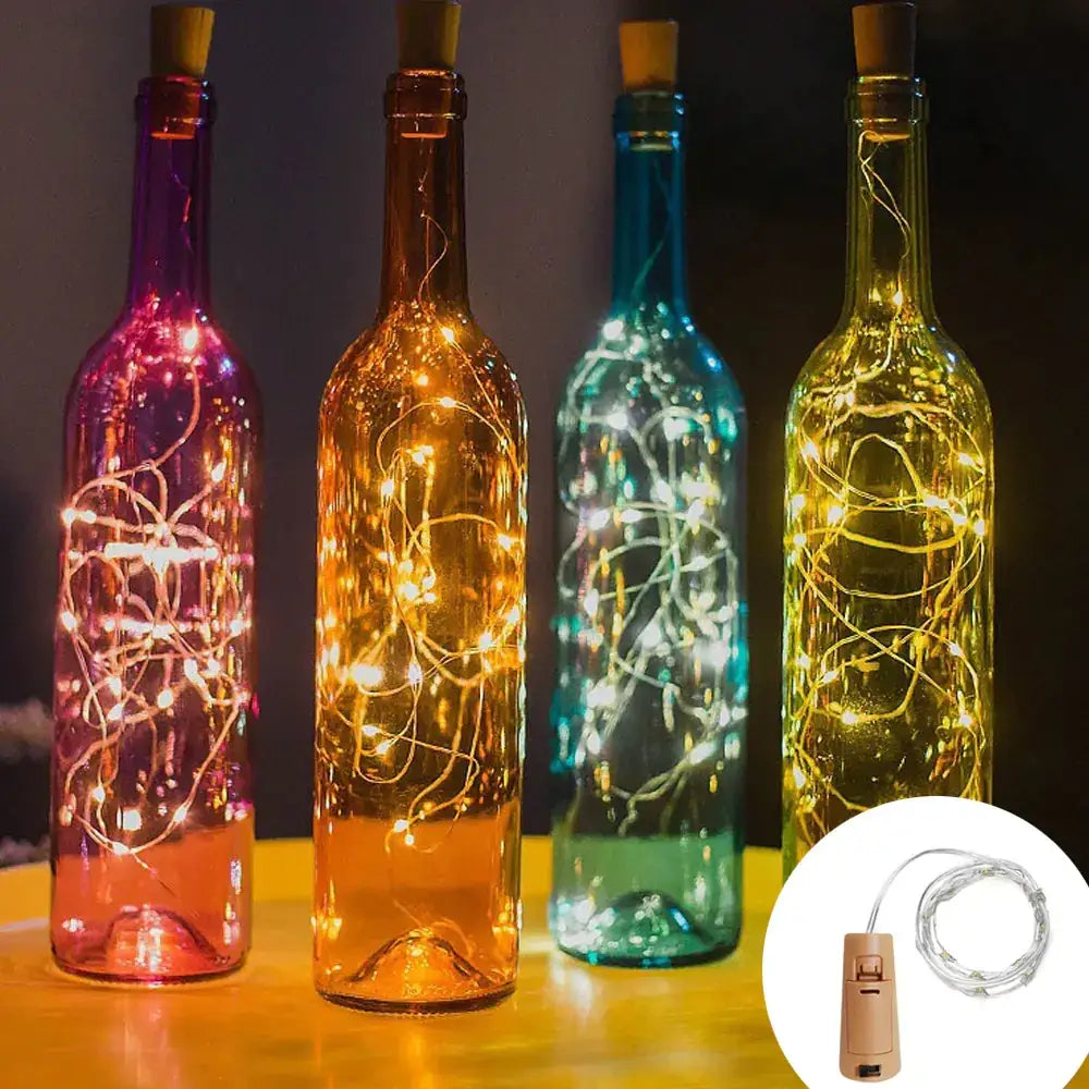 Four colorful glass wine bottles, each containing a string of warm-toned led fairy lights and sealed with a cork stopper.