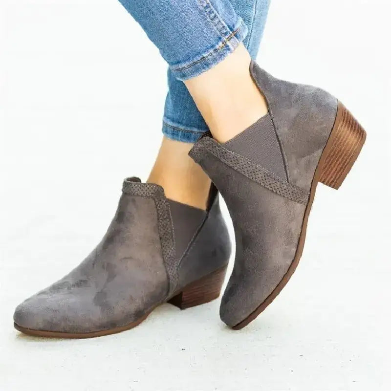 Gray suede ankle boots with a low wooden block heel and decorative woven strap detail.