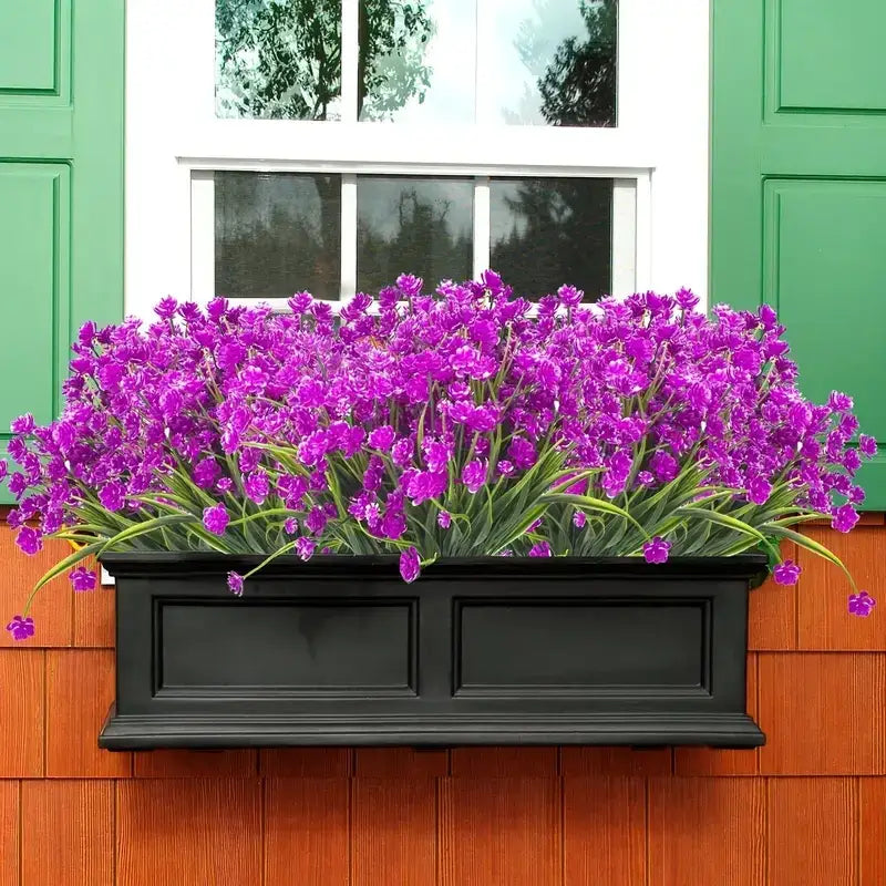Black rectangular window box filled with vibrant purple artificial flowers and green stems.