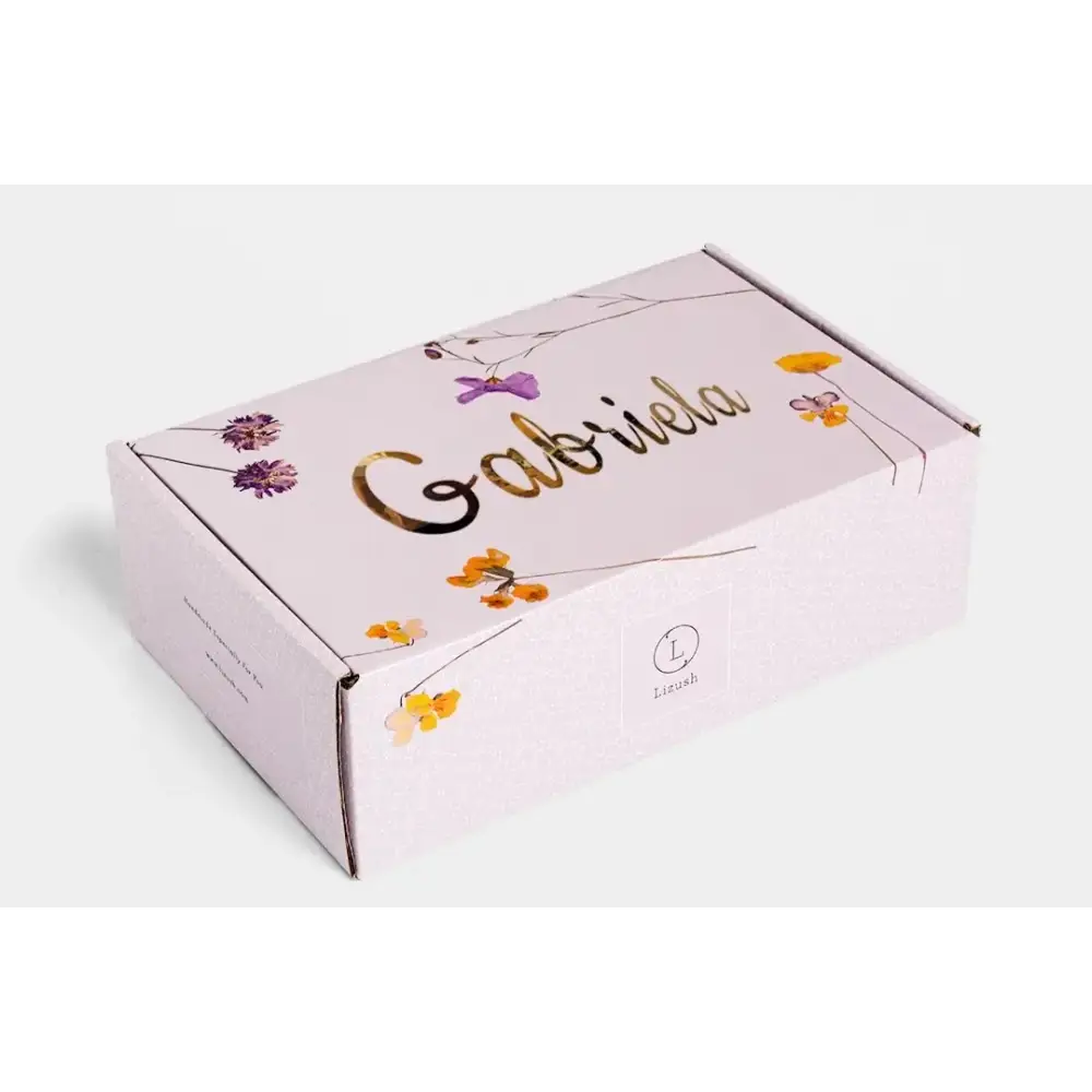 A delicate lavender-colored cardboard box adorned with gold foil lettering and a floral design featuring purple and yellow blossoms.