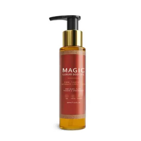 A sleek amber glass bottle of magic luxury body oil with a gold-tone pump dispenser and an elegant red label featuring intricate golden patterns.