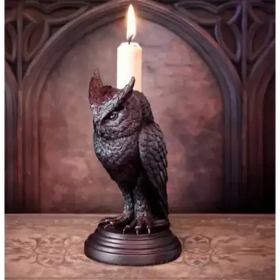 Dark bronze owl candle holder with intricate feather detailing and a lit white candle perched on its back.