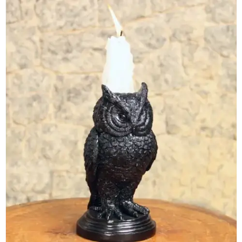 Black owl-shaped candle holder with a white wax candle lit atop its head.