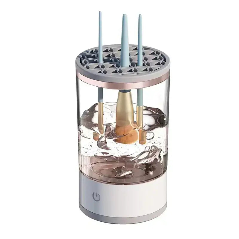 Transparent cylindrical brush cleaner with a white base, gray top ring holding light blue handles of brushes submerged in water.