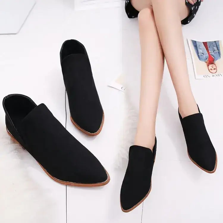 Black suede slip-on ankle boots with a pointed toe and light brown rubber sole.
