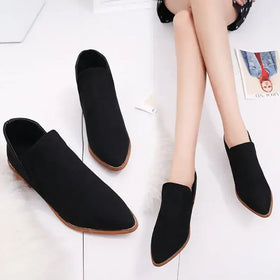 Black suede slip-on ankle boots with a pointed toe and light brown rubber sole.