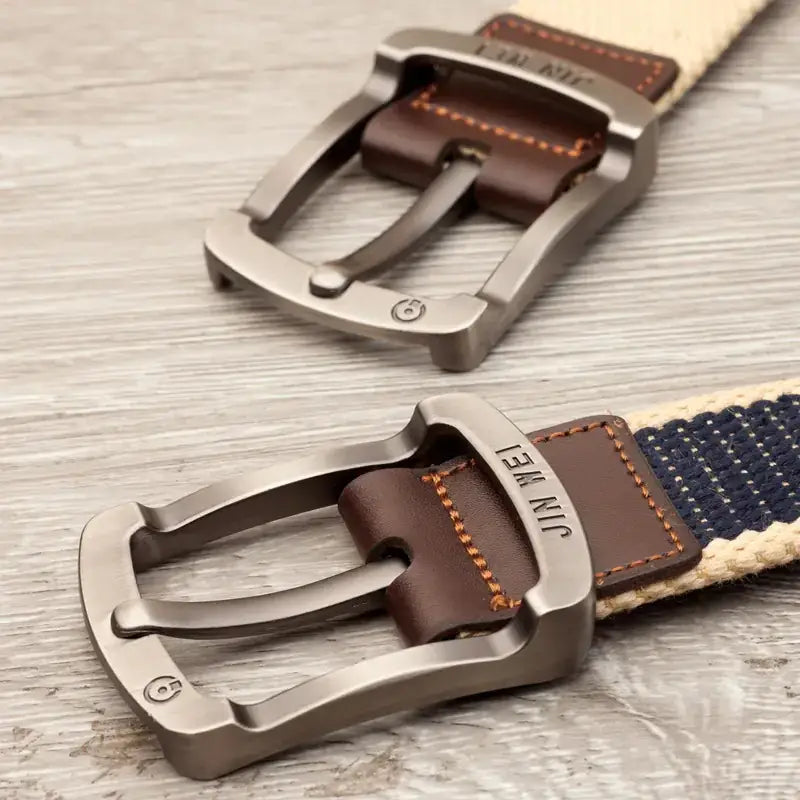Silver-toned metal belt buckle with brown leather accents and orange stitching, attached to a woven fabric strap.