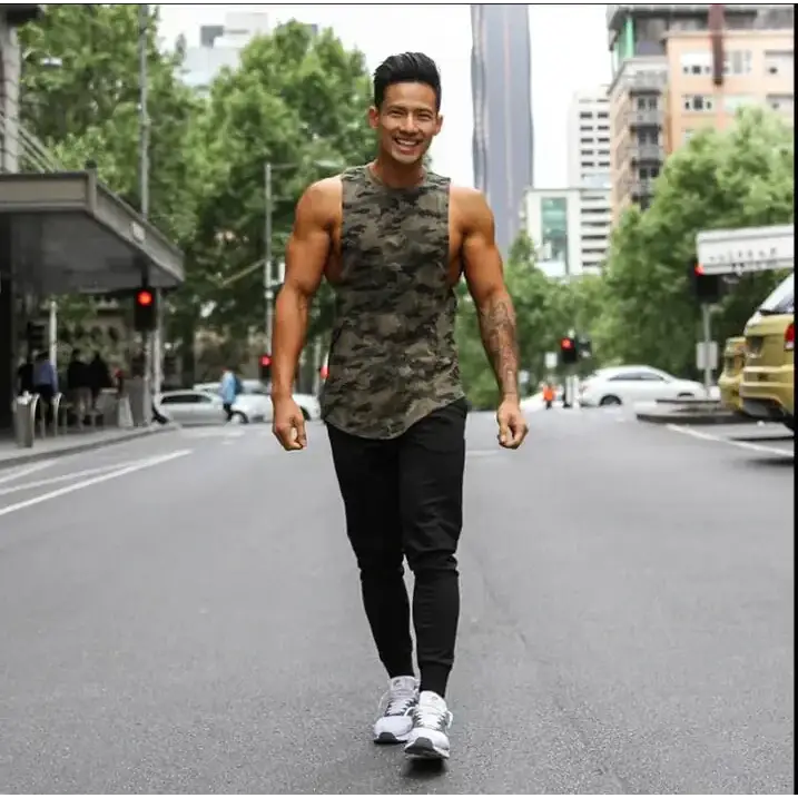 A muscular man wearing a camouflage-patterned sleeveless tank top and black pants.