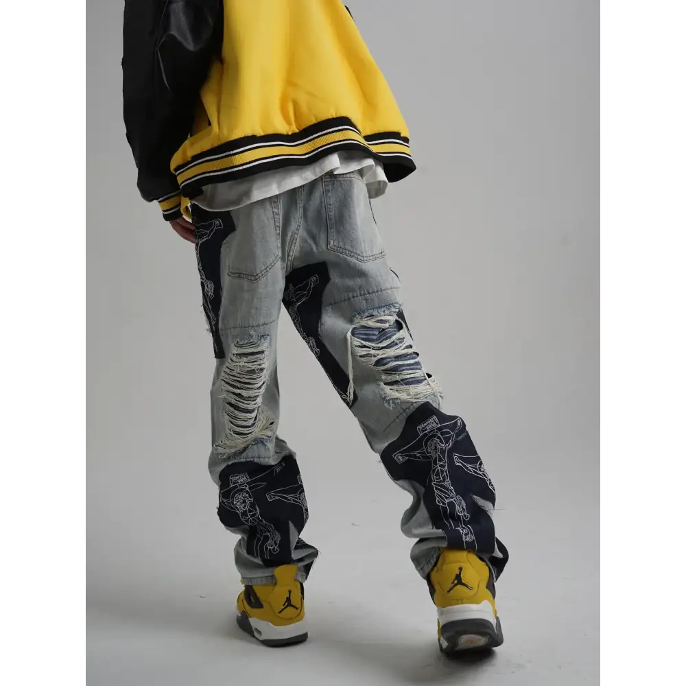 Distressed light-wash denim pants with bold black panels featuring white line-art graphics and ripped detailing.