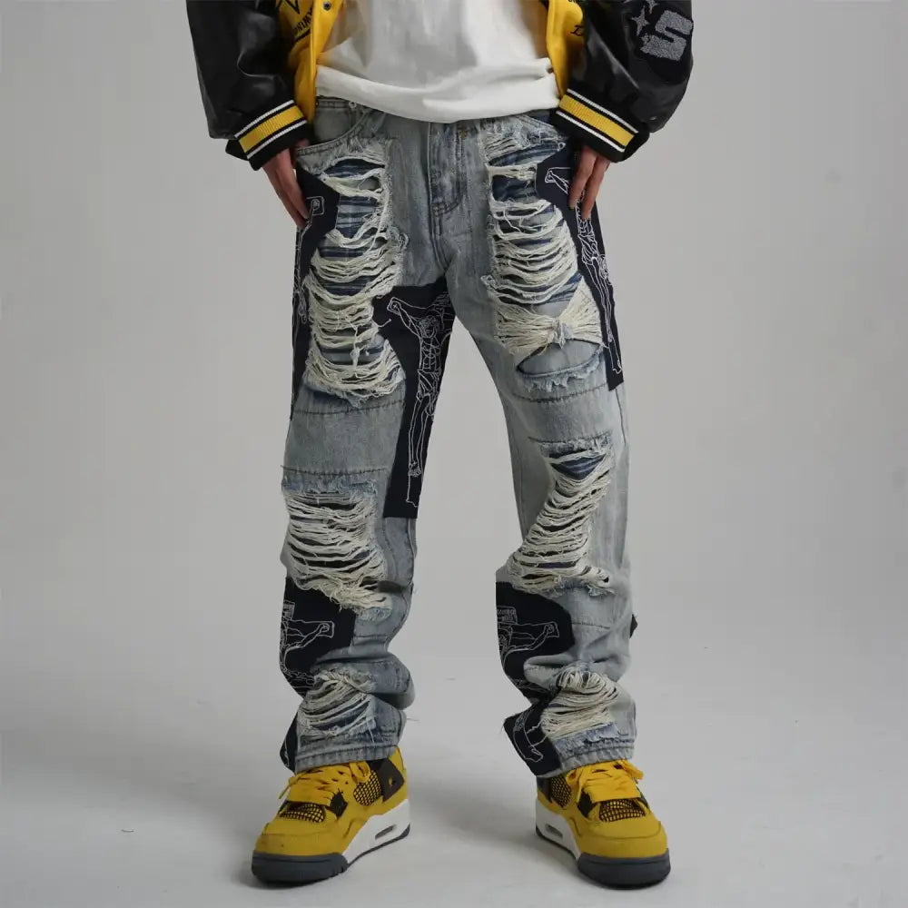 Distressed light-wash denim jeans featuring bold black graphic patches and frayed, ripped detailing along the legs.