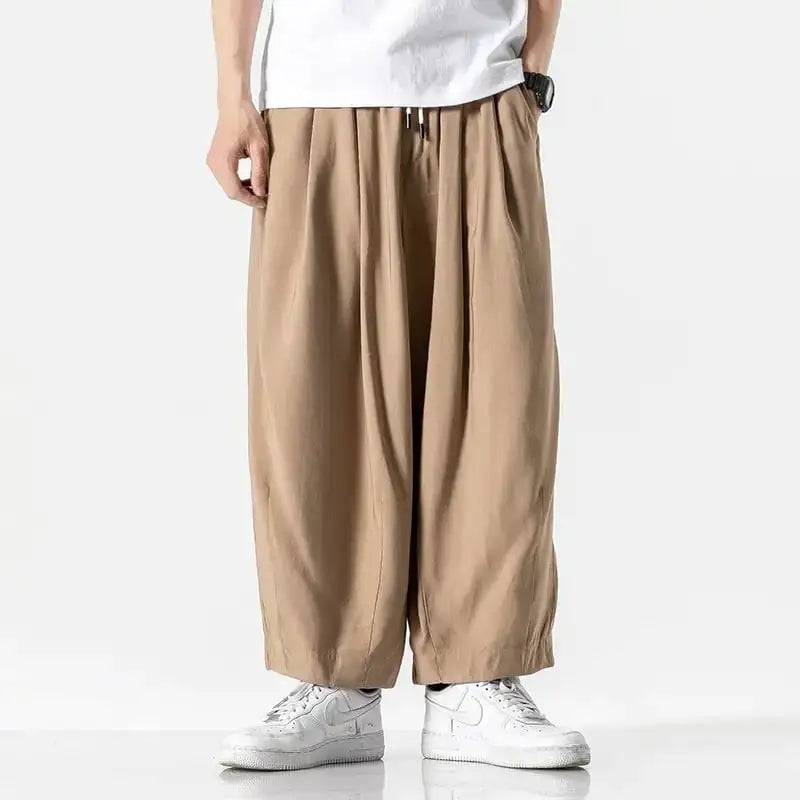 Beige, loose-fitting cotton trousers with a drawstring waist and tapered legs.