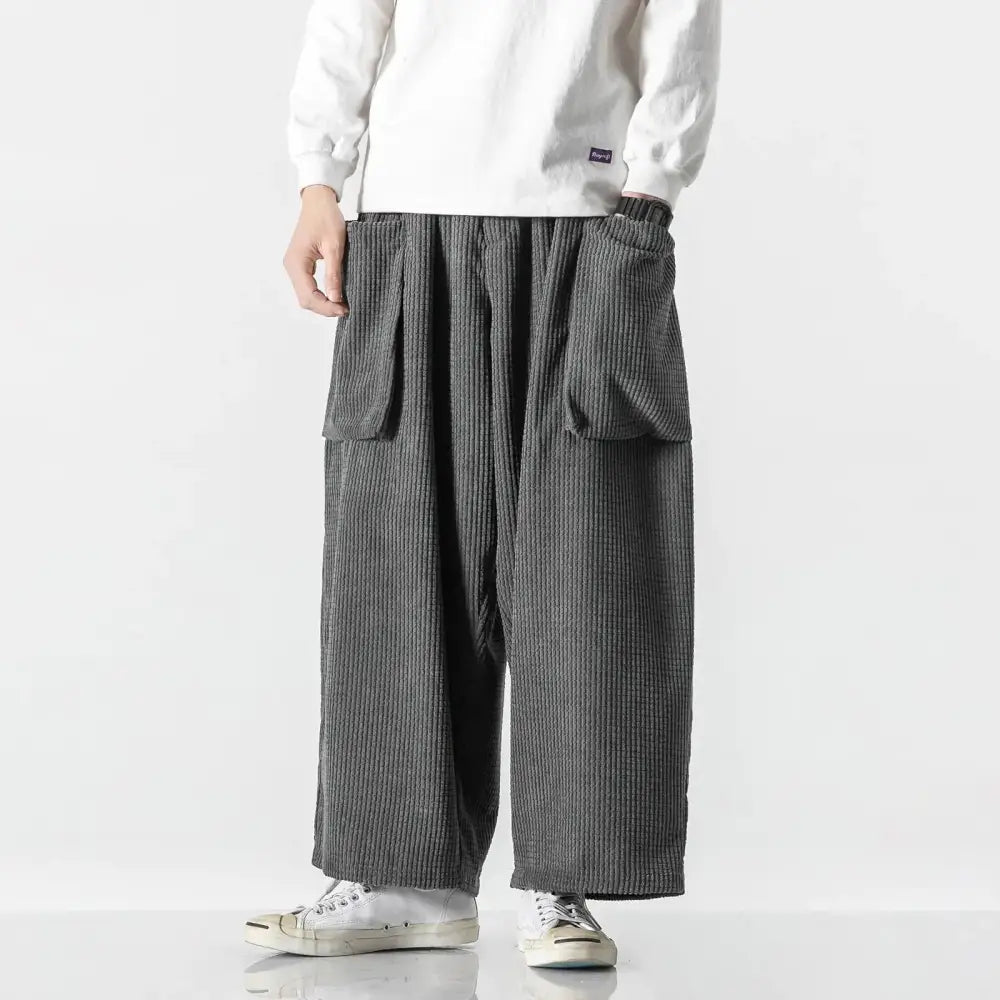 Dark gray corduroy pants with a relaxed, wide-leg cut and large side pockets.