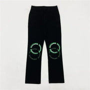 Black pants featuring green and white embroidered text in circular patterns on each knee.