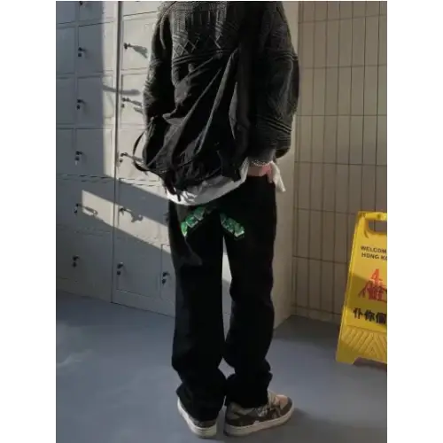 Black denim jeans with green embroidered patches at the back pockets.