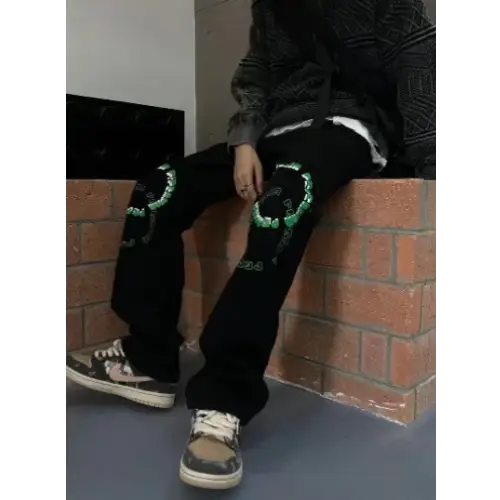 Black jeans with green embroidered skull designs on the knees.