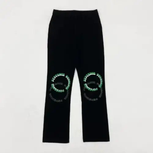 Black velvet pants featuring green and silver beaded circular logos on each knee.