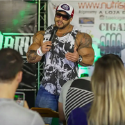 A muscular man wearing a white and red pro house cap, black sunglasses, and a sleeveless hoodie with a bold black-and-white skull pattern.