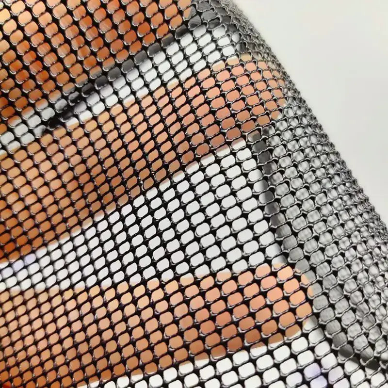 A shimmering metallic mesh fabric with a repeating pattern of interlocking oval links in alternating copper and silver tones.