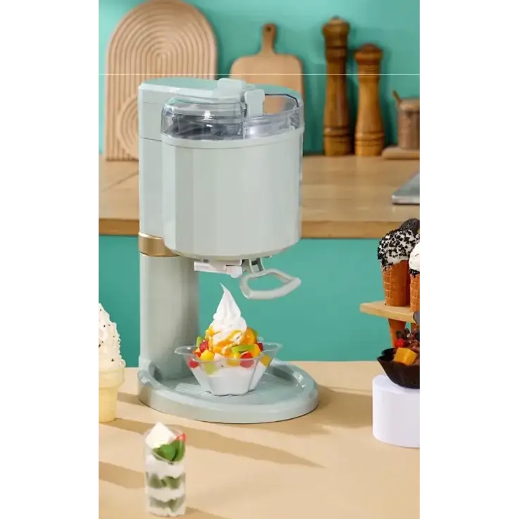 Pastel green countertop ice cream maker with a clear lid and white handle dispensing swirls of creamy dessert into a glass bowl.