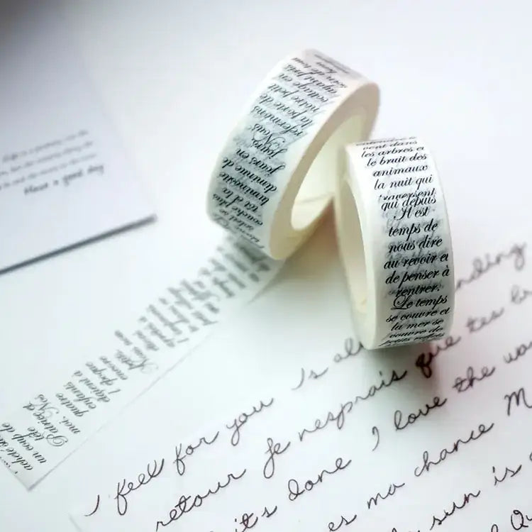 Two rolls of white washi tape with black french script printed on them, resting atop a sheet of handwritten letter paper.