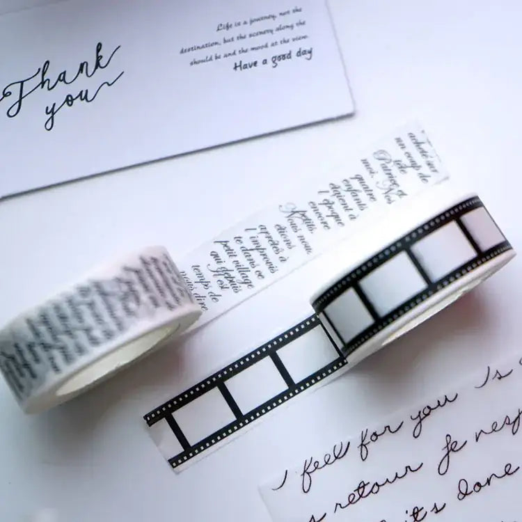 Two rolls of washi tape, one with black cursive script on a white background and the other featuring a classic film strip design in black and white.