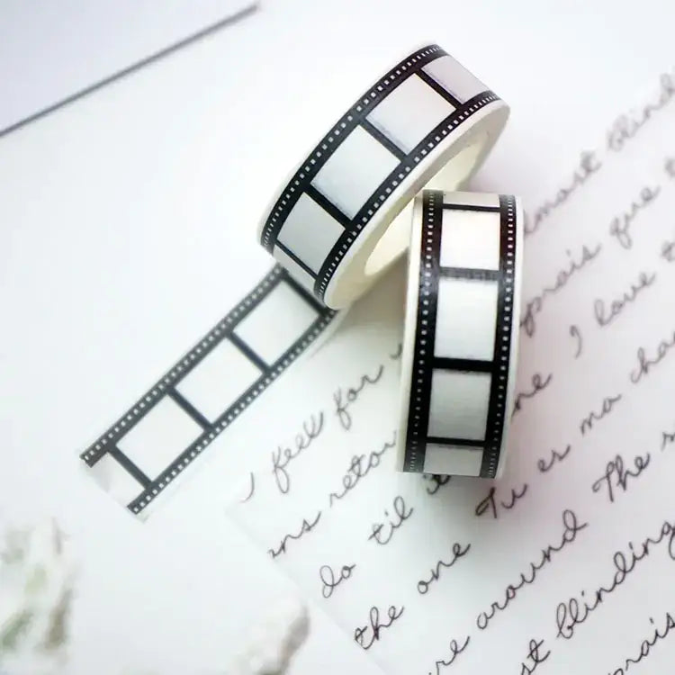 Two rolls of black and white filmstrip-patterned washi tape, one partially unrolled to reveal its adhesive side.