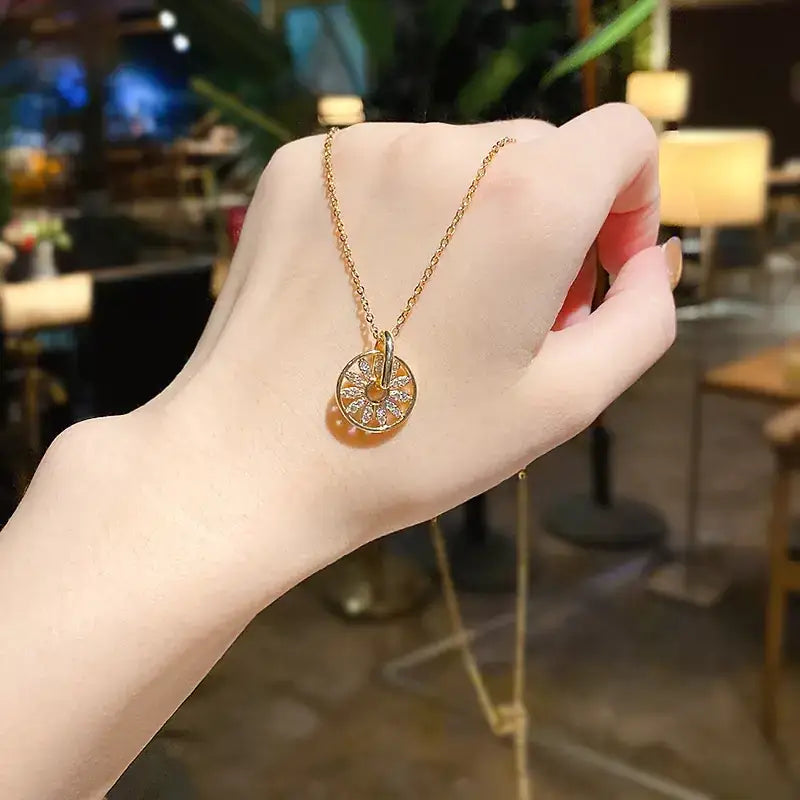 Gold-toned necklace with a circular pendant featuring intricate diamond-like embellishments and a central loop design.