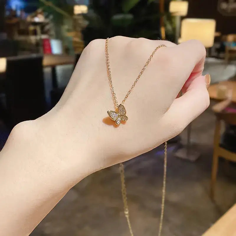 A delicate gold-toned butterfly pendant necklace with sparkling clear stones set in a pave design, suspended on an elegant chain.