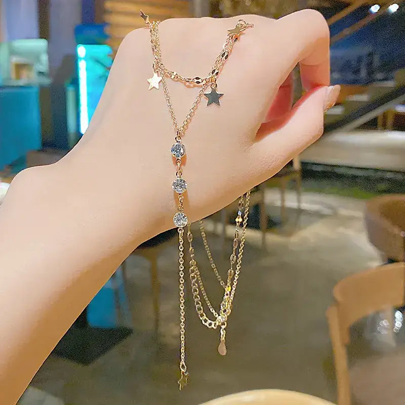 A delicate gold-toned layered bracelet adorned with sparkling clear crystals and dangling star-shaped charms.
