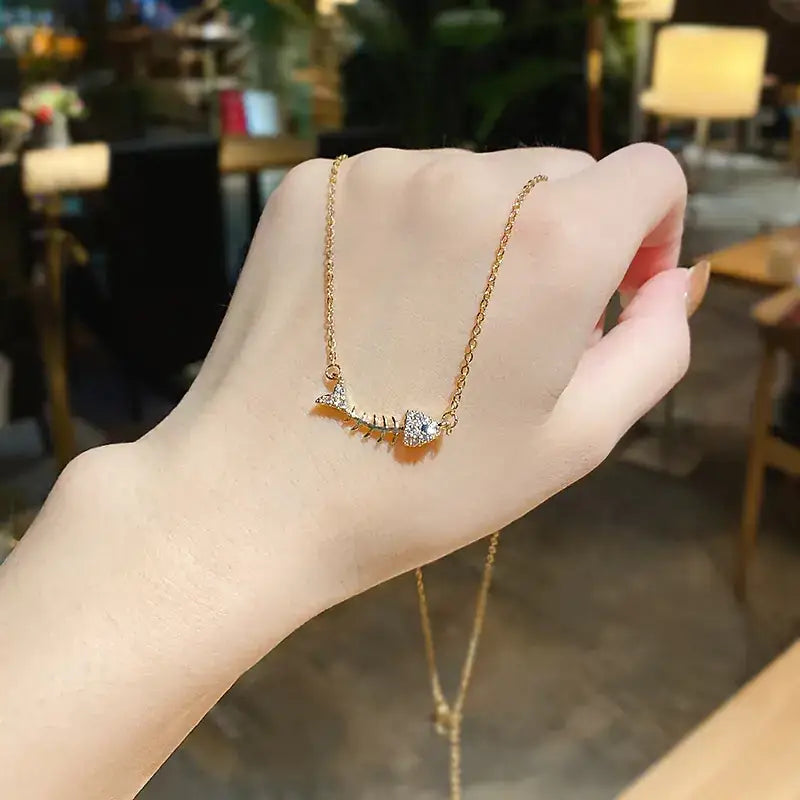 A delicate gold chain necklace featuring a small, sparkling fishbone-shaped pendant adorned with clear crystals.