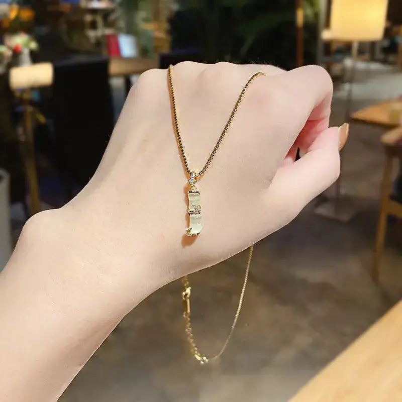Gold chain necklace with a delicate, translucent jade pendant featuring intricate engraved patterns and small diamond accents at the top.