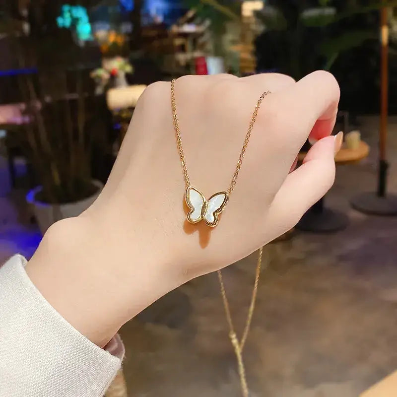 Gold chain necklace with a butterfly pendant featuring white enamel wings and gold-tone edges.