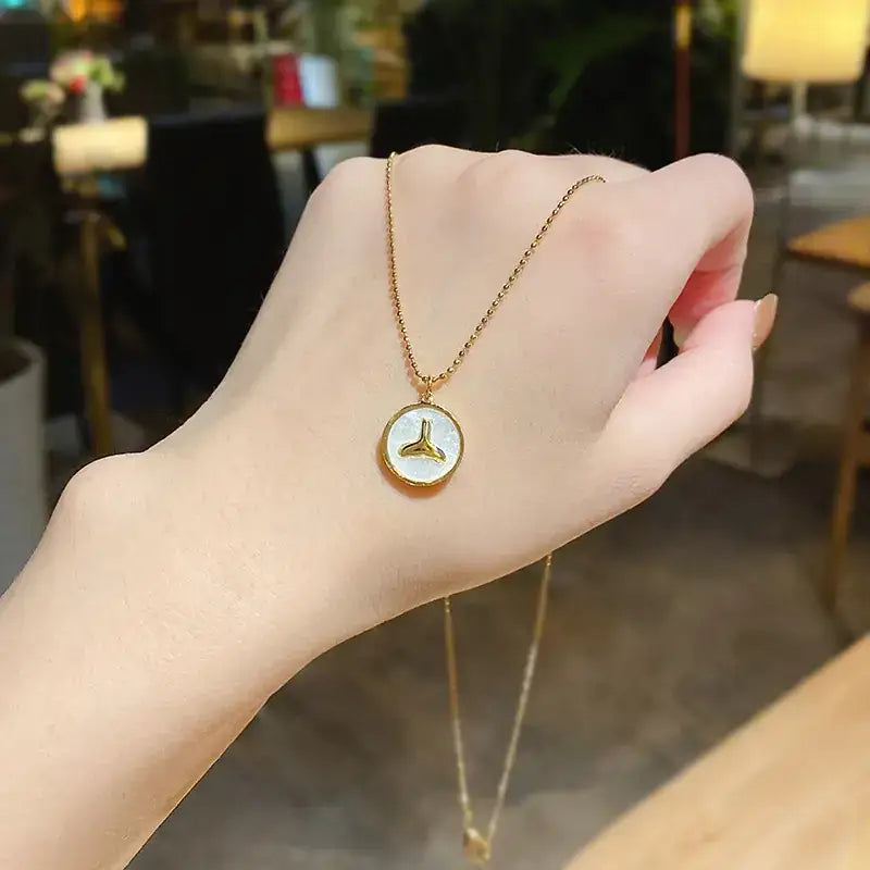 Gold chain necklace with a circular pendant featuring a white mother-of-pearl center and a gold-trimmed triangular design.