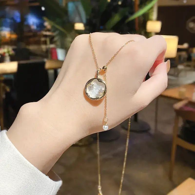 Gold-toned necklace with a circular pendant featuring an iridescent mother-of-pearl center and small diamond accents, suspended from a delicate chain.