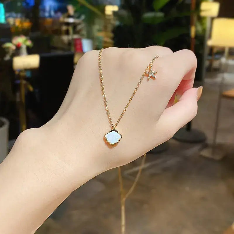 Gold chain necklace featuring a white shell-shaped pendant and a small star charm with sparkling stones