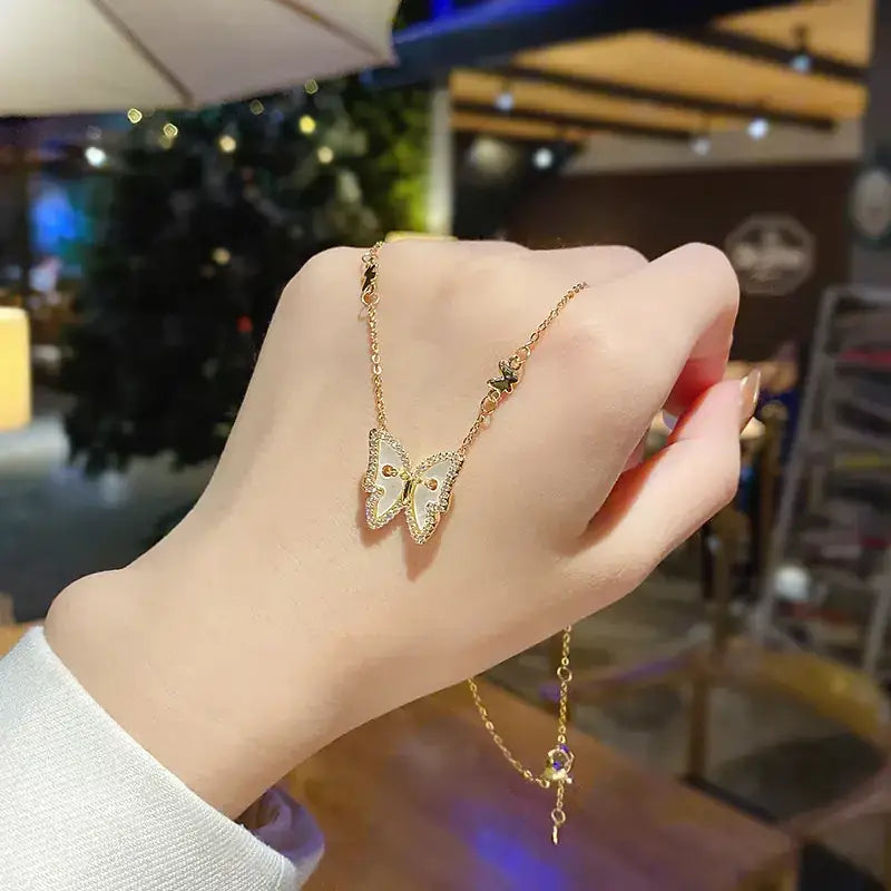 A delicate gold-toned butterfly pendant necklace with sparkling rhinestones and a small purple gemstone accent.