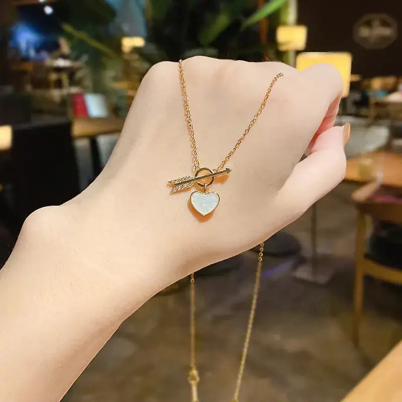Gold chain necklace with a heart-shaped pendant and an arrow charm, featuring a white opal-like center on the heart.