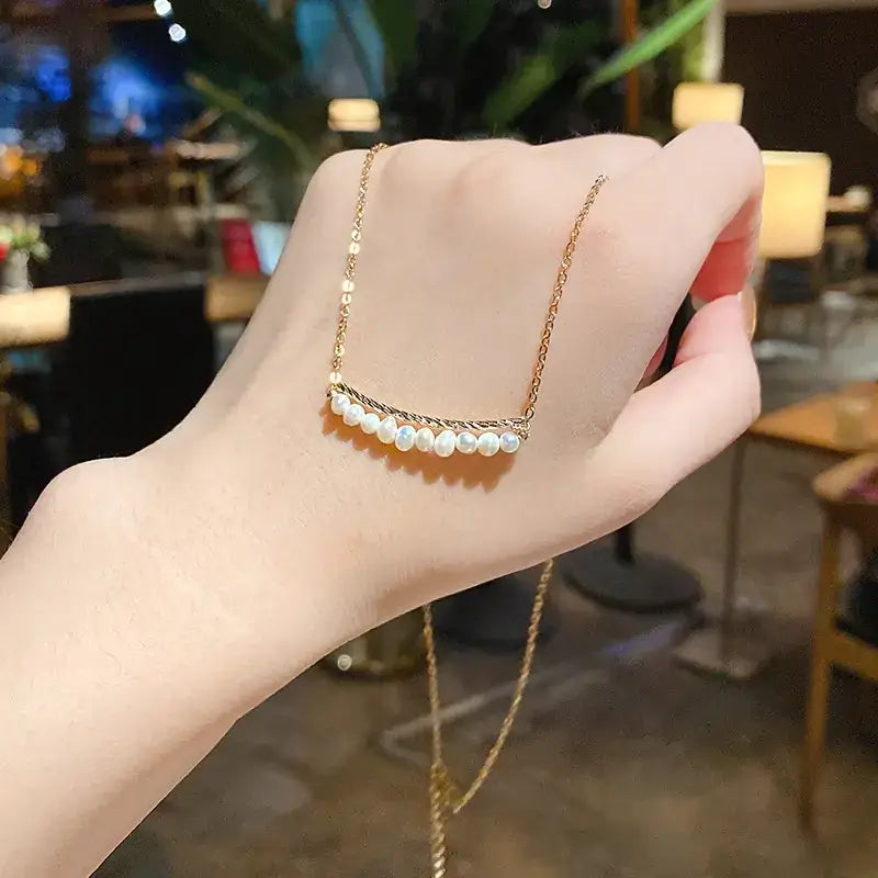 A delicate gold-toned necklace featuring a curved bar adorned with evenly spaced, lustrous white pearls.