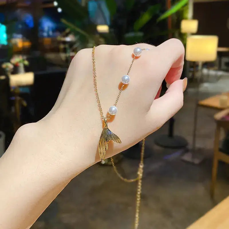 Gold-toned mermaid tail pendant necklace with three white pearls along the chain.