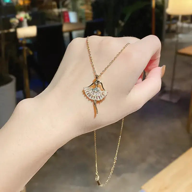 Gold-toned ballet dancer pendant necklace with a sparkling, fan-shaped skirt adorned with clear crystals and an accent blue gemstone at the center.