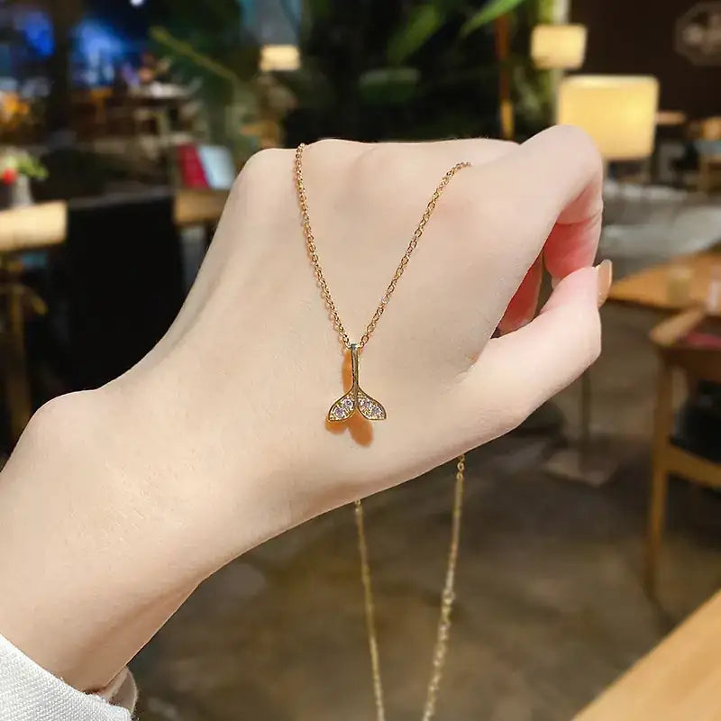 A delicate gold-toned necklace featuring a small, sparkling mermaid tail pendant adorned with clear crystals.