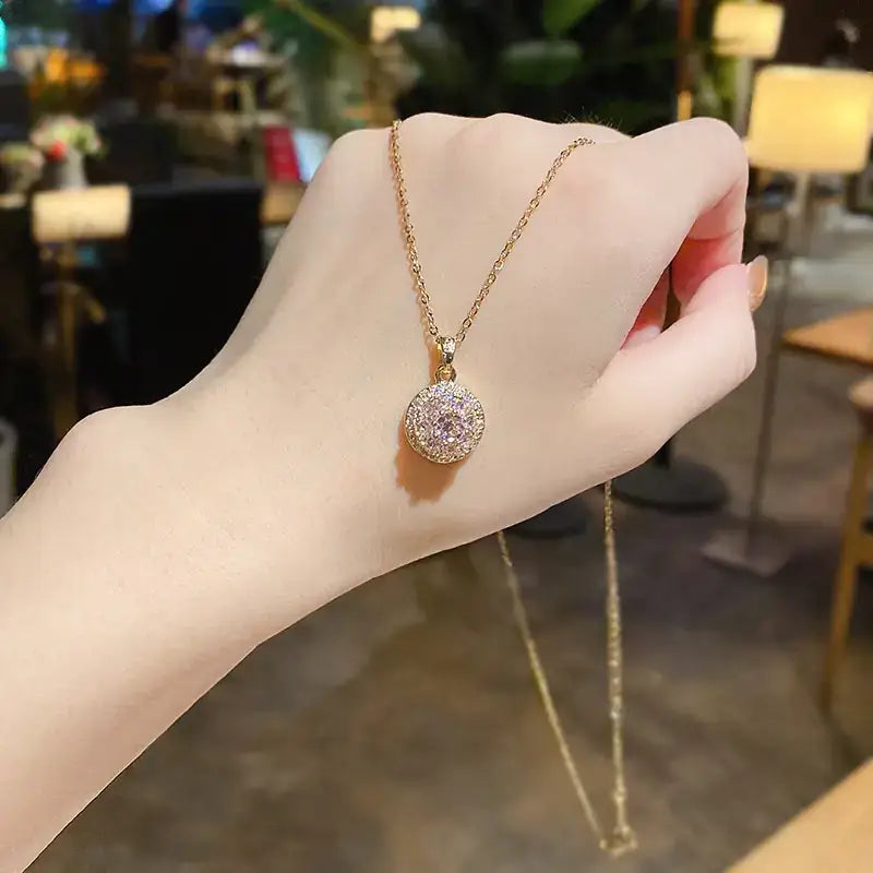 A delicate gold-toned necklace featuring a round, sparkling pendant adorned with numerous clear and pinkish crystals.