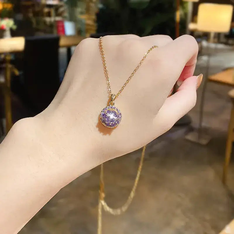 A delicate gold chain holds a round pendant featuring a sparkling purple gemstone encircled by smaller clear crystals.
