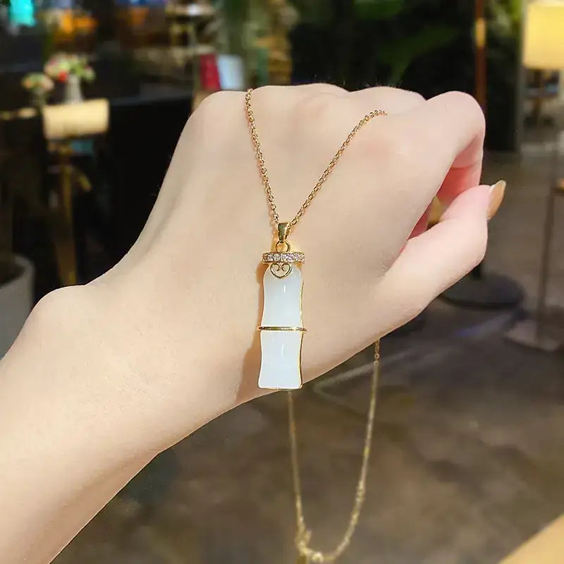 A delicate gold chain holds a pendant shaped like a bamboo stalk, featuring two smooth white jade segments separated by a golden band and adorned with small diamonds around the top.