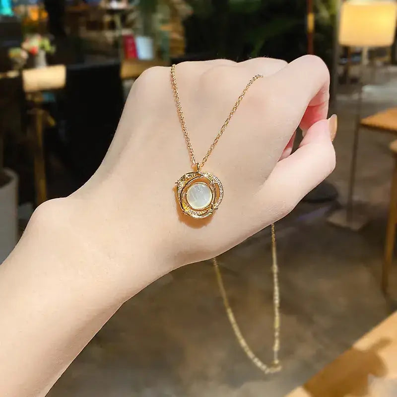 Gold-toned necklace with a circular pendant featuring an oval-shaped, milky white moonstone surrounded by sparkling clear stones and intricate gold detailing.